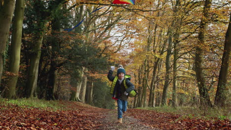 Kleiner-Junge,-Der-Spaß-Daran-Hat,-Auf-Dem-Weg-Durch-Die-Herbstliche-Landschaft-Zu-Laufen-Und-Drachen-Steigen-Zu-Lassen