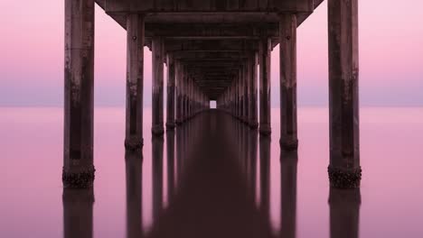 a serene sunset view beneath a pier: capturing tranquility and reflection at dusk over calm waters with graceful architecture and vibrant colors