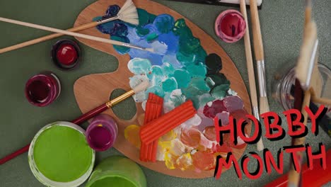 Animation-of-hobby-month-text-in-red-over-oil-paints,-paintbrushes-and-palette-on-green-table-top