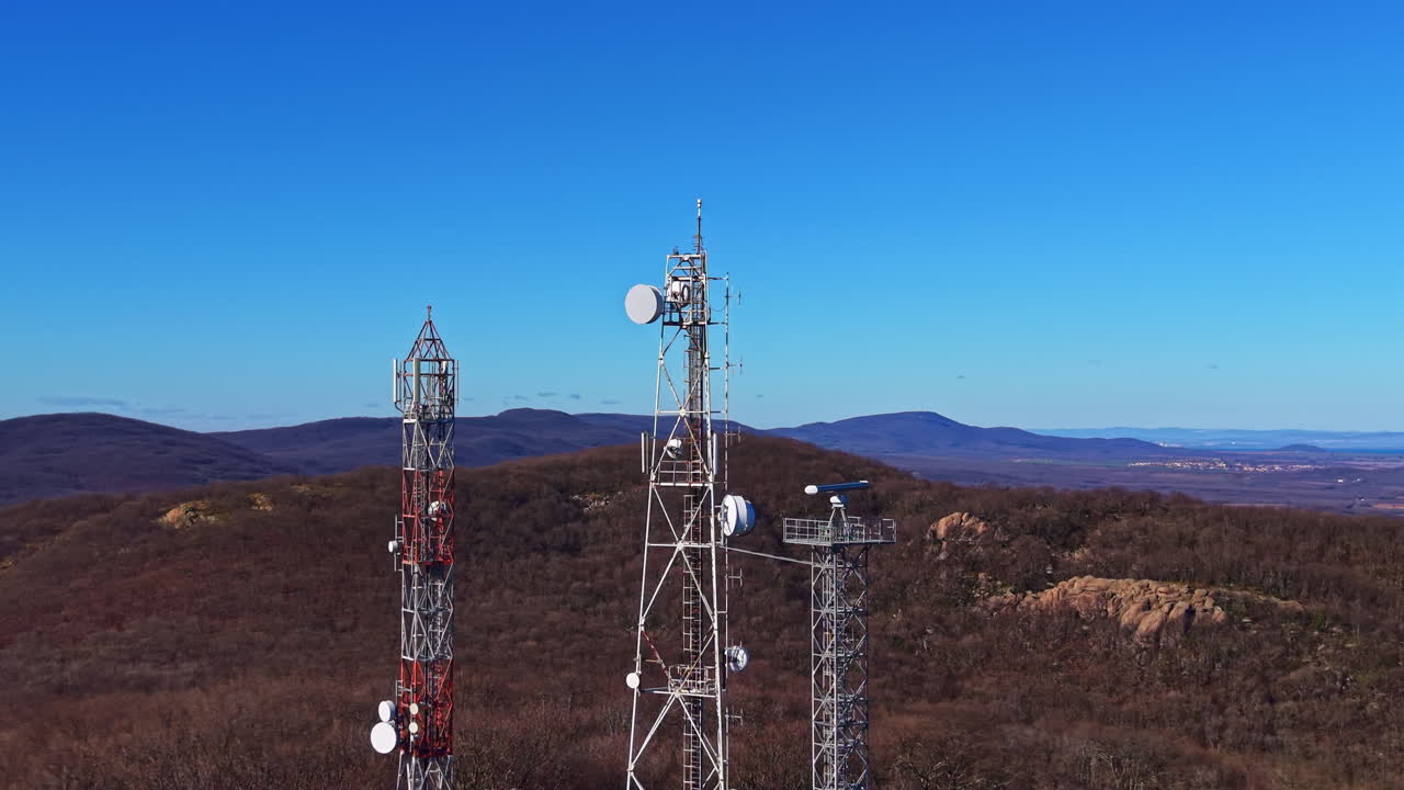 Torri di telecomunicazioni su una montagna durante una giornata serena in una zona rurale con cielo azzurro e colline distanti visibili sullo sfondo