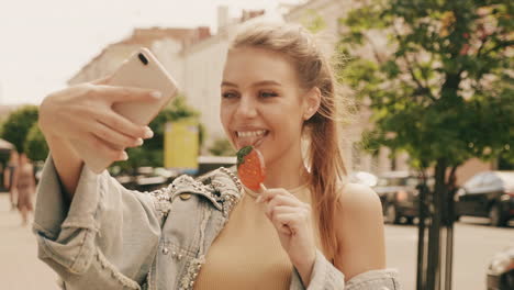 woman taking selfie with lollipop on city street