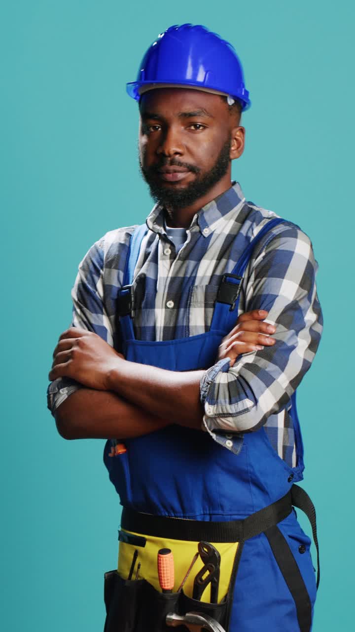 Vertical video: Cheerful smiling handyman standing over blue backdrop