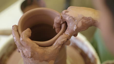 over shoulder view of potter working wet clay rotating on workshop pottery wheel