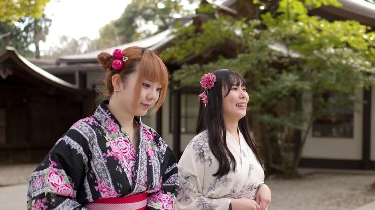 Due giovani donne giapponesi in kimono floreali camminano e parlano fuori da un santuario shintoista