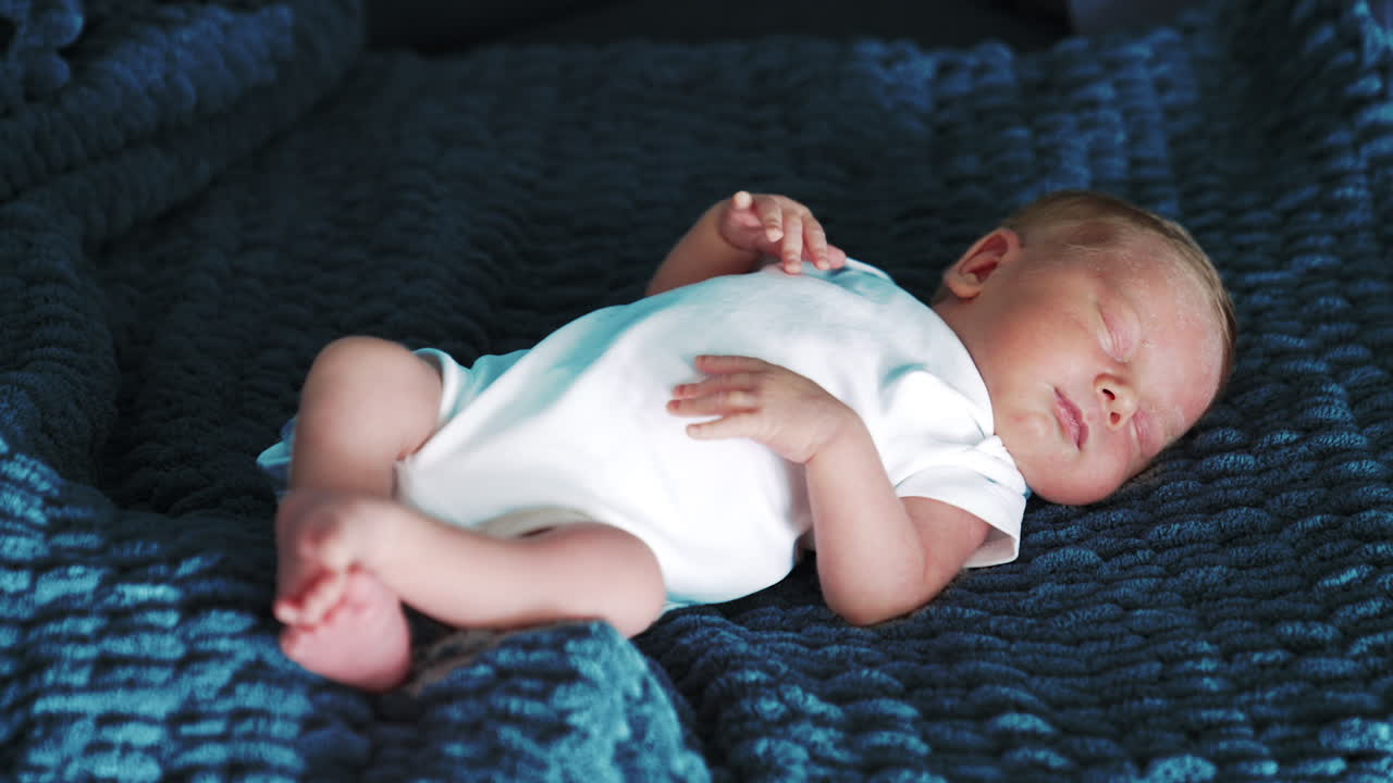 Peaceful sleeping baby wearing white bodysuit. Blond newborn resting on the blue plaid. Close up.