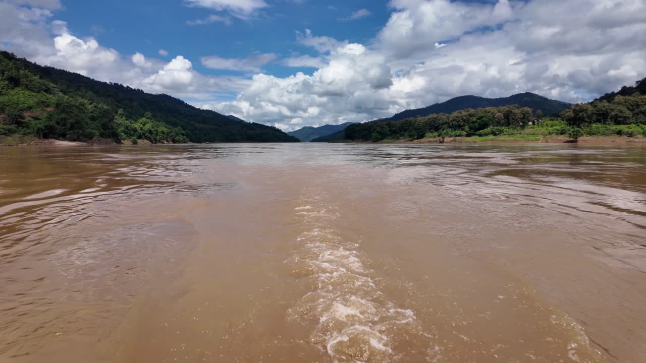 Mekong River boat wake trailing through muddy water surrounded by green mountains