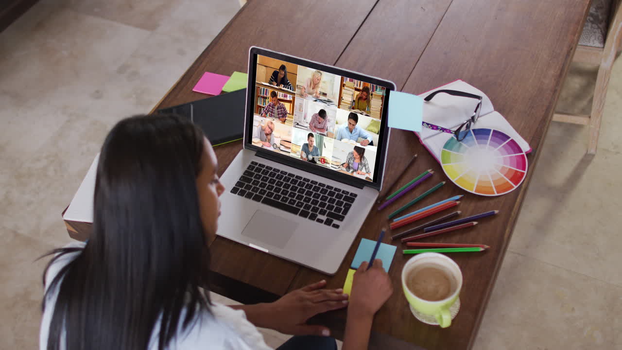 Maestra caucásica usando una laptop en videollamada con estudiantes, tomando notas