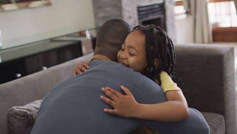 feliz hija afroamericana abrazando a su padre en la sala de estar