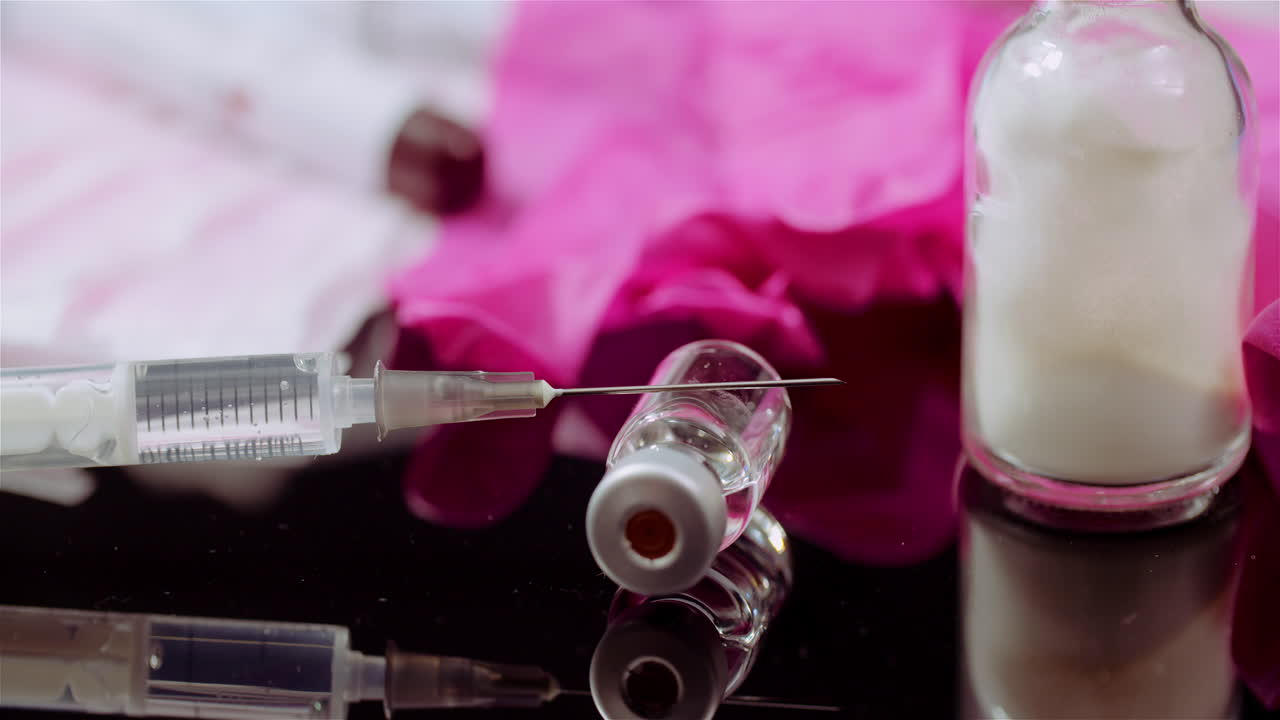 Sprøjte og hætteglas med medicin på en reflekterende overflade.