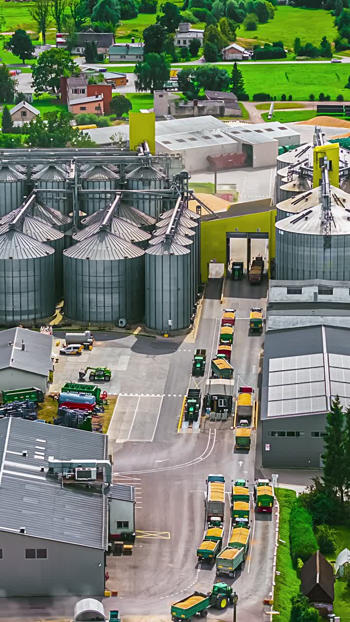 Grain silos and processing facility with trucks offloading and exiting through weighing station, vertical
