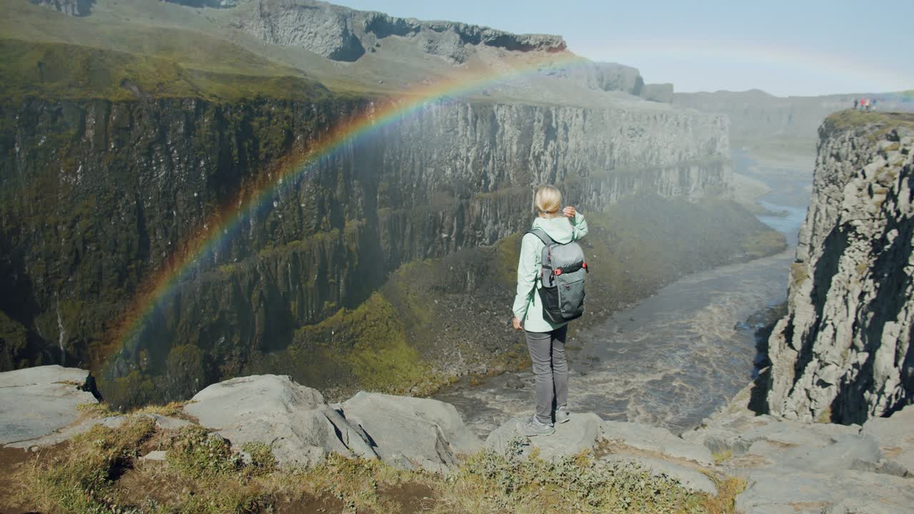 mujer de pie en el borde de un acantilado mirando hacia el cañón con el río cerca de la cascada de detifoss en islandia