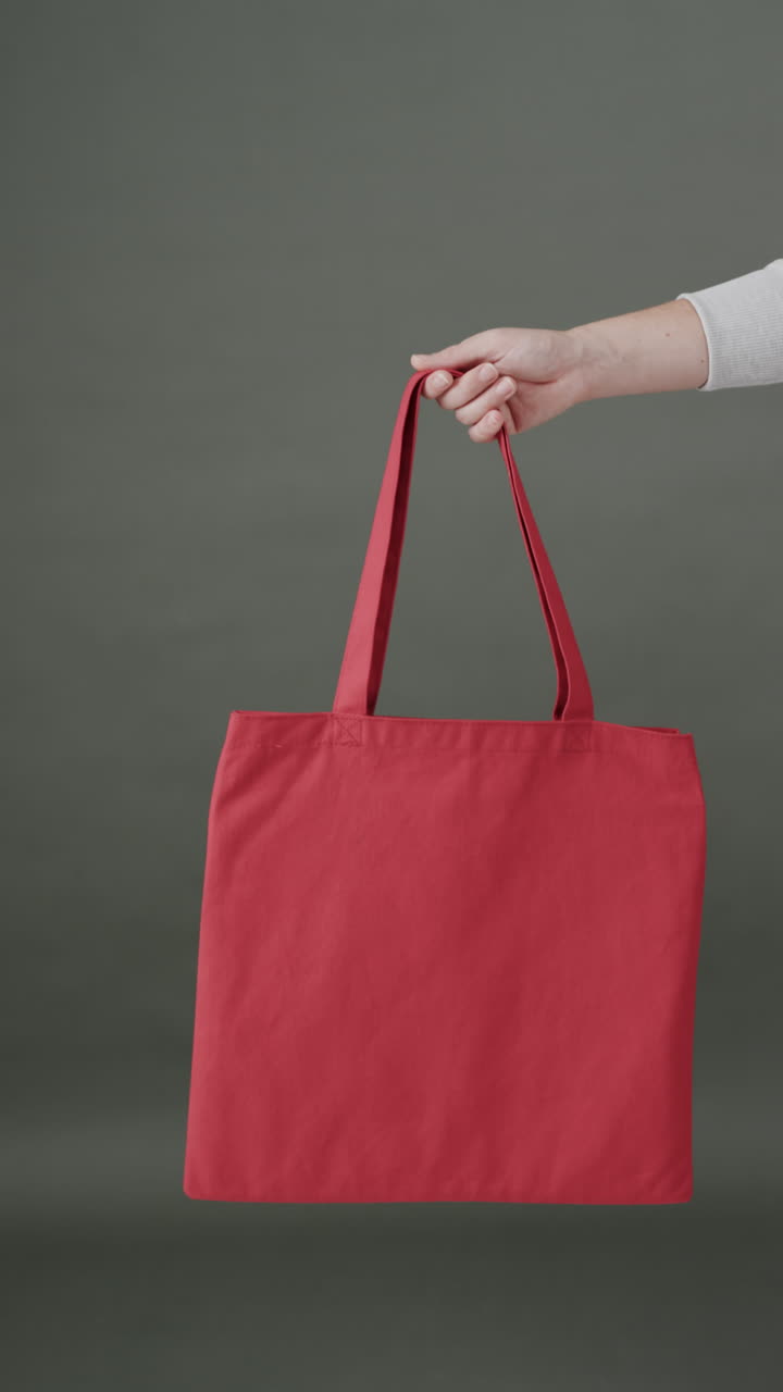 Vertical video of hand of caucasian woman with red canvas bag and copy space on grey background