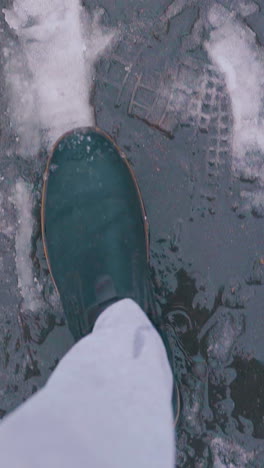 hurrying man in grey pants and black leather boots walks fast along street with slush and snow close vertical view