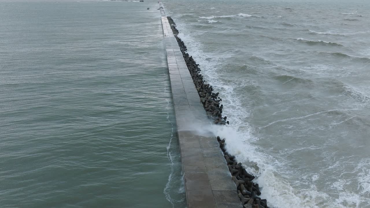 Aerial establishing view of Port of Liepaja concrete pier , autumn storm, big waves splashing, overcast, wide birdseye drone shot moving forward