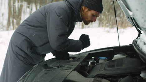 man stuck in the winter forest holding a torch and checking his car engine problem