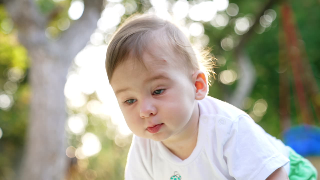 Adorable baby looking surprised staring into camera. Toddler turns around in the rays of setting sun. Blurred backdrop.