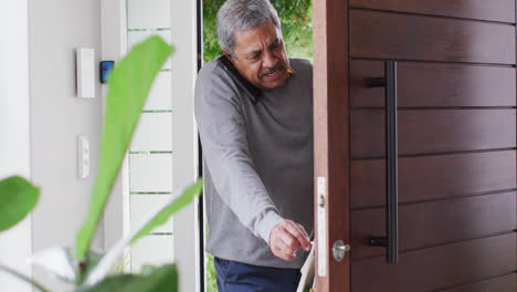 Busy-senior-biracial-man-coming-home-with-groceries-and-talking-on-smartphone