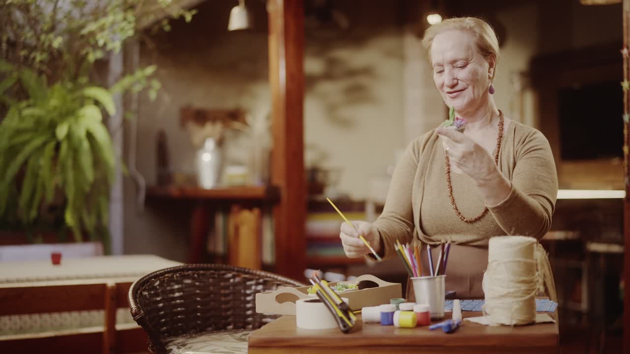 Donna anziana sorridente che crea o dipinge un piccolo oggetto con materiali artistici