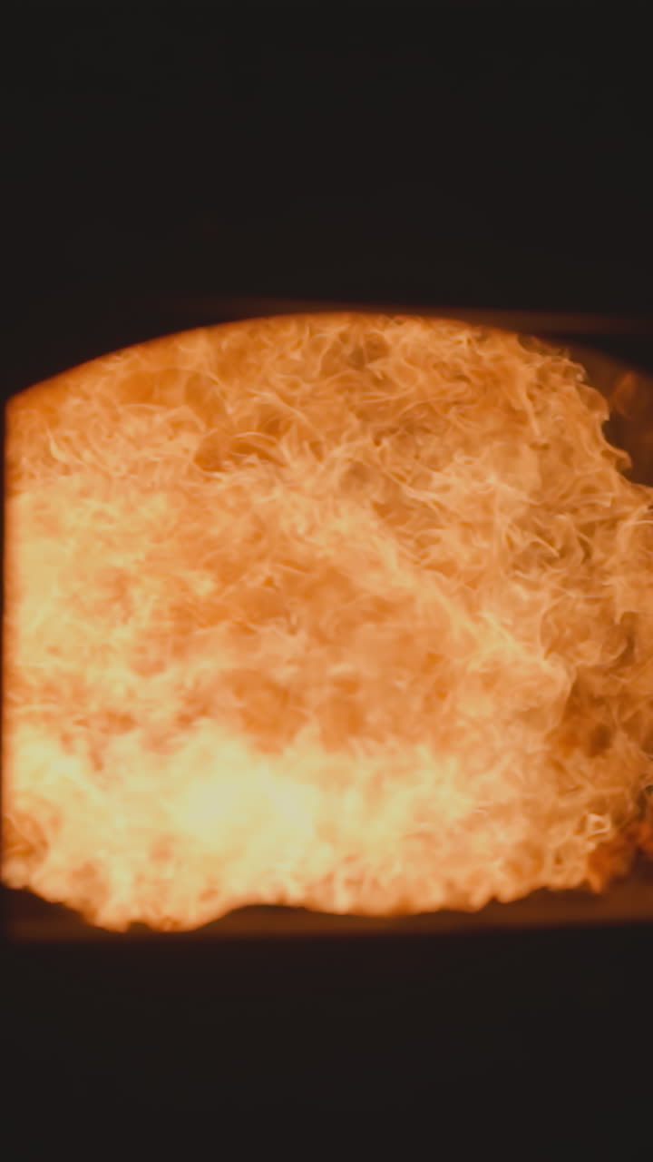 Orange flame tongues in metal melting industrial furnace with open door in dark factory workshop. Direct heater equipment used at metalworking plant