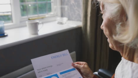 mujer anciana en silla de ruedas con factura de energía de ee.uu. por radiador en el costo de la vida crisis energética