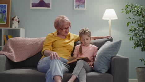 grandmother with granddaughter reads book in living room