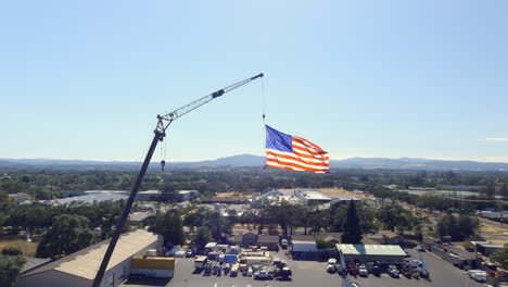 Aerial,-American-USA-flag-hanging-from-extended-fire-truck-ladder-during-the-day