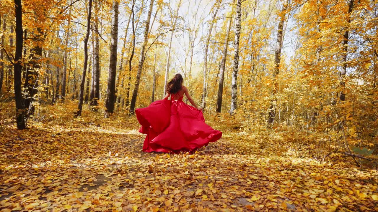 A Woman Dressed in a Flowing Red Dress Twirls Gracefully Through a Sunlit Autumn Forest, Surrounded by Vibrant Yellow and Orange Leaves, Evoking a Sense of Freedom and Joy