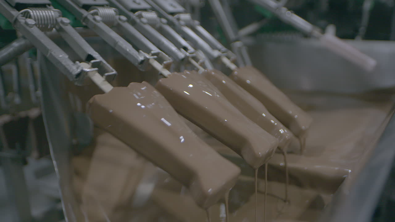 Food production assembly line dipping ice cream lollies into melted chocolate