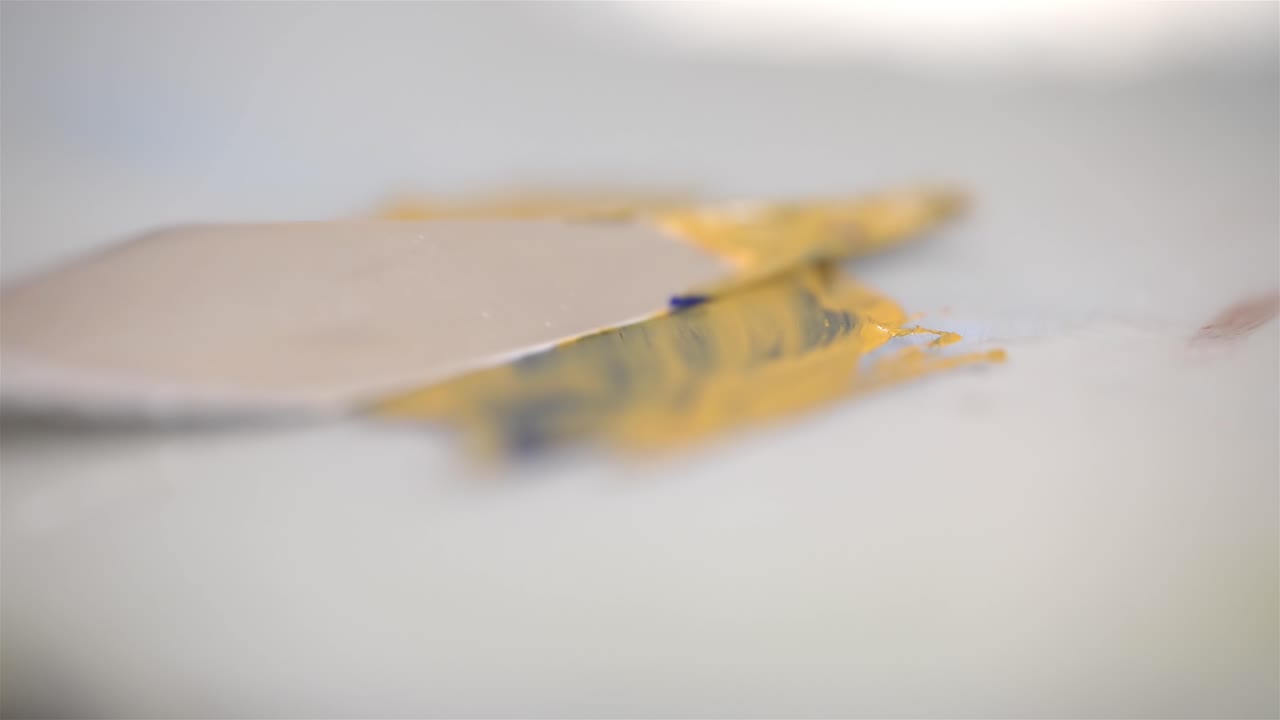 예술가들의 팔레트 칼은 오렌지 오일 페인트에 대해 파란색을 퍼뜨리고 그것을 혼합합니다.