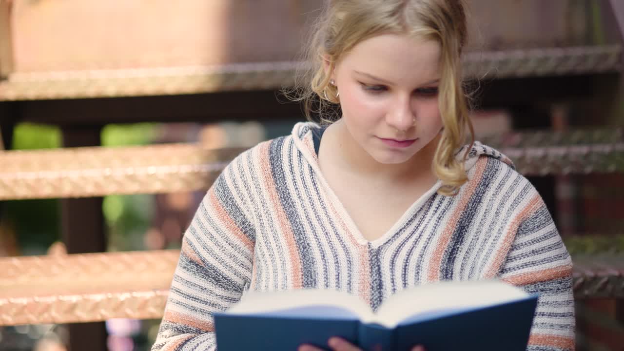 Nahaufnahme einer Studentin, die eine Seite umblättert, während sie draußen auf einer Treppe ein Buch liest.