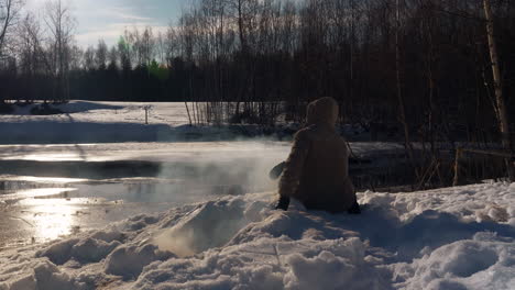 man checks on campfire dug into snow