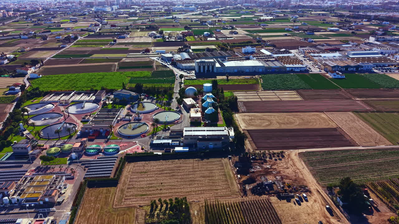 Overview of a water treatment facility near a farming area with various tanks and fields during daytime