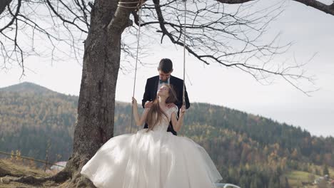 Newlyweds.-Caucasian-groom-with-bride-ride-a-rope-swing-on-a-mountain-slope