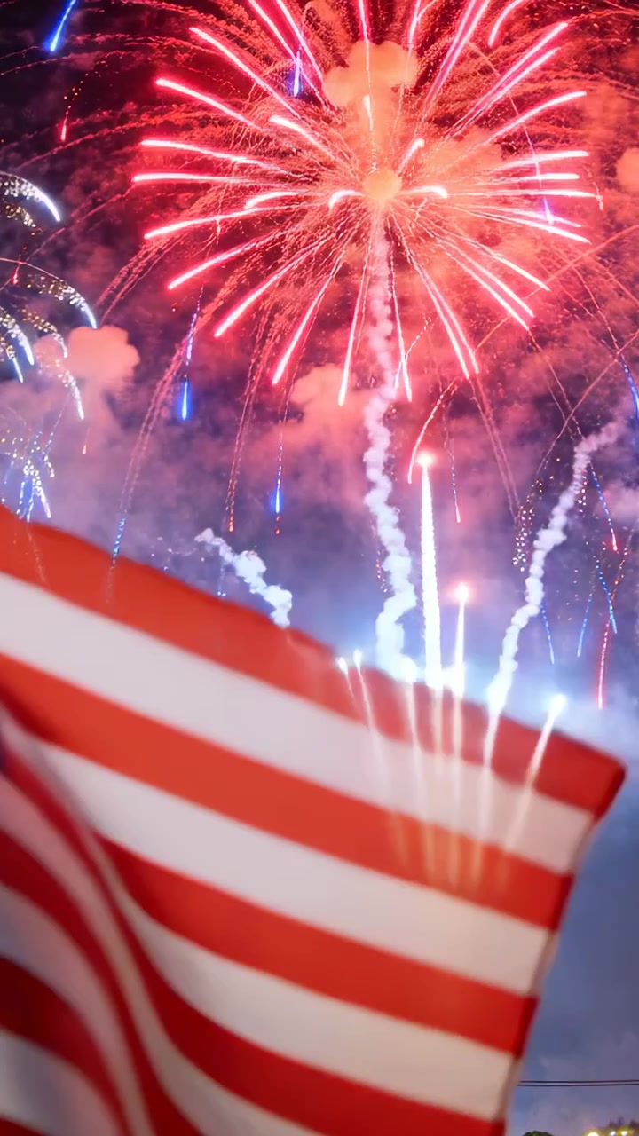 Vertical video: Launching shells causing US flag flapping at night, fireworks bursting with smoke