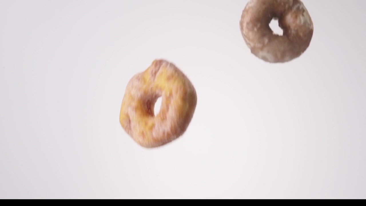 Assorted glazed and chocolate donuts raining down on white seamless backdrop in cinematic slow motion. donut shop branding, coffee chain ads, office breakfast catering posts.