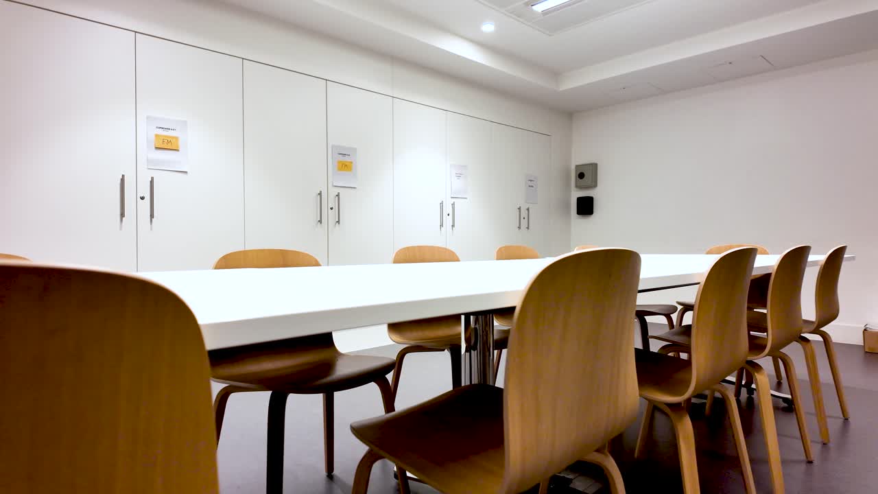 Interni moderni di una sala riunioni con lungo tavolo da conferenza bianco e sedie in legno per presentazioni aziendali e sessioni di collaborazione di gruppo