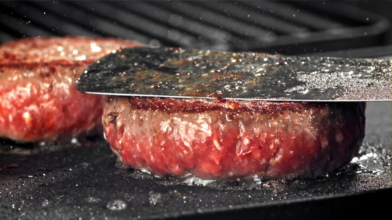 Nærbillede af rå burgerbøffer, der syder på en varm grill