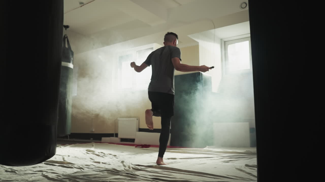 Sportsman jumps on rope in combat gym. Strong boxer does exercises with skip rope in martial arts club slow motion. Leg muscles training techniques