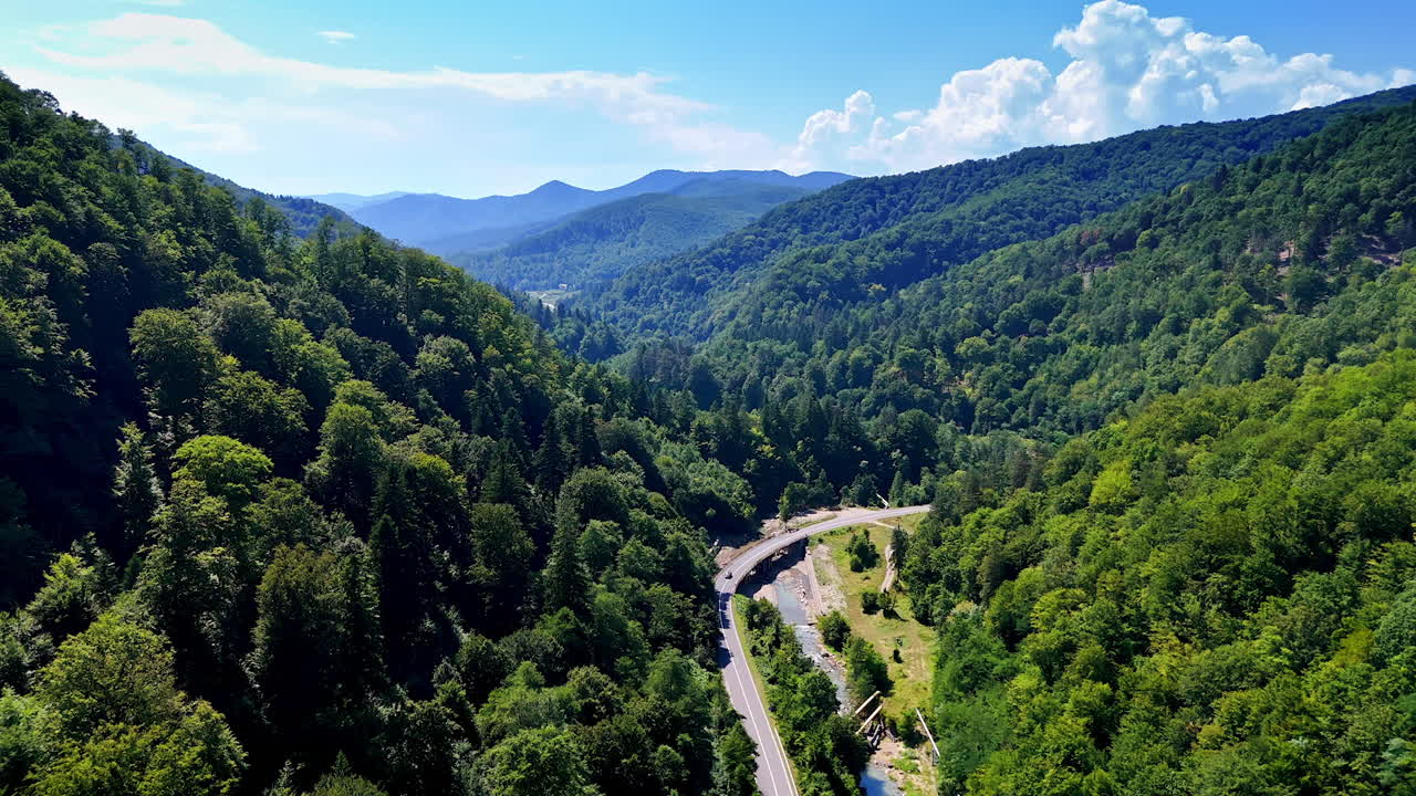 Mountain road winding through dense forest in Carpathians. Drone view of winding mountain road surrounded by dense green forest in the Carpathian Mountains, Romania