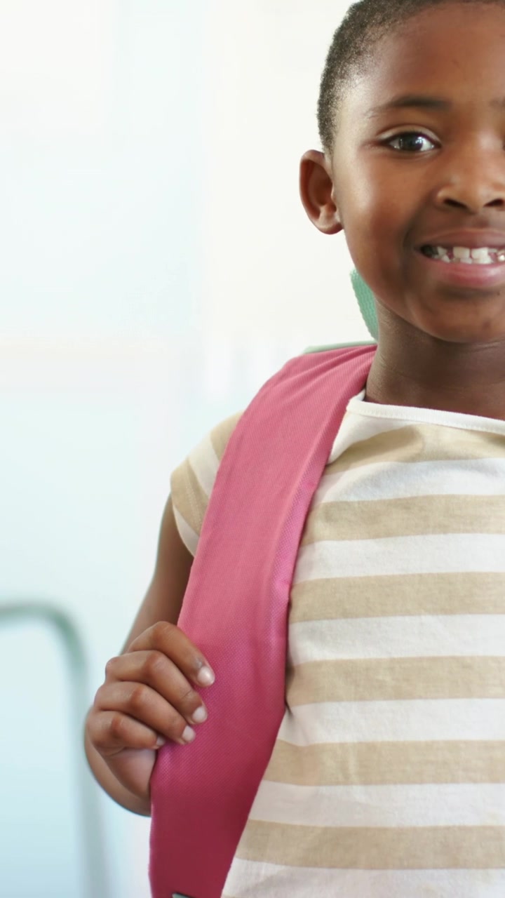 Vertical video: Smiling student in beige shirt holding pink backpack strap at school, copy space