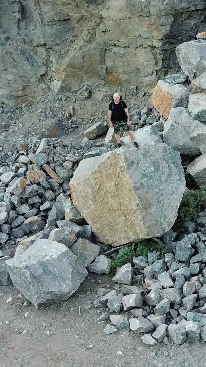 Aerial view of a young man standing on a rock. Traveler looks at the locality ahead of him. Travel concept. Vertical video