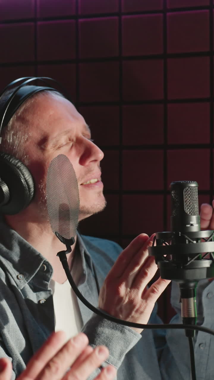 Two men wearing headphones, one in a black cap and hoodie and the other in a blue shirt and white undershirt, are clapping hands in a soundproof recording studio. They are mid-performance