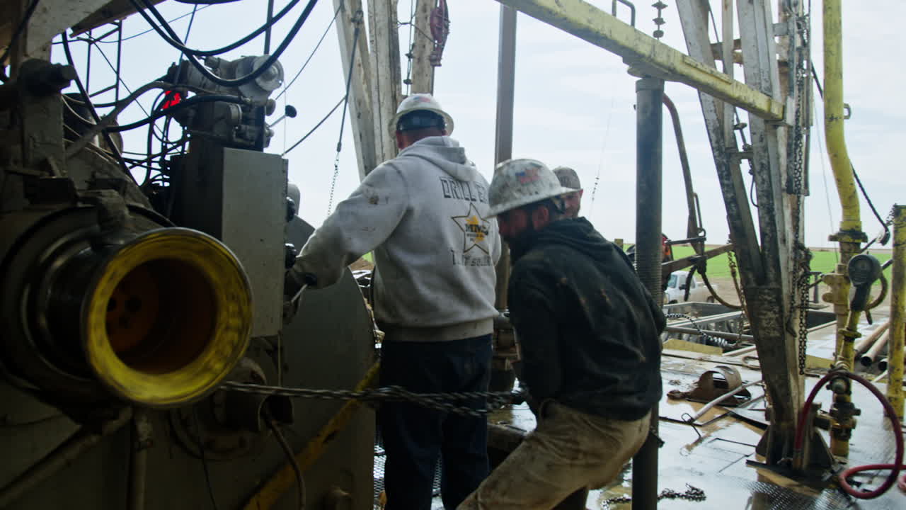 Group of men working at the location for drilling the natural resources. Workers in helmets arrange the diverse equipment for boring.