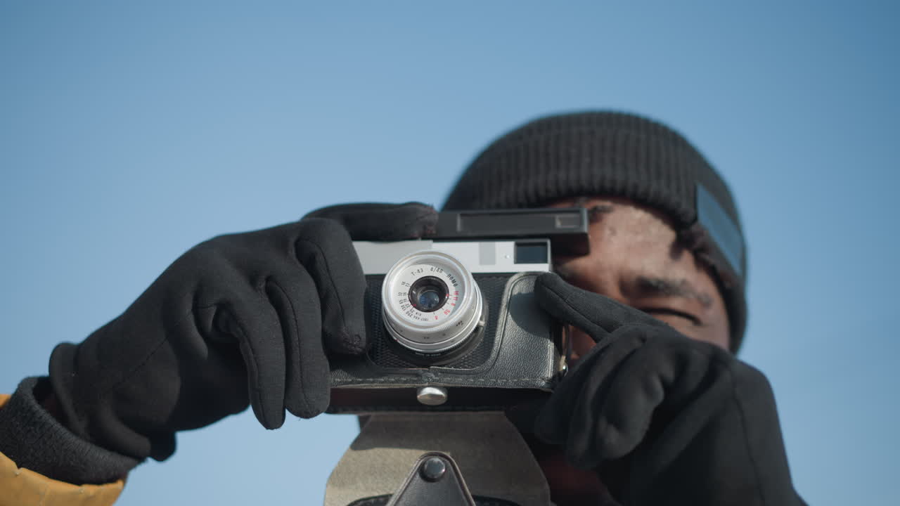camera lifted up by reporter in winter coat and gloves, single hand tweaks lens, shoots photo, reviews shot under bright sky on snowy city street, capturing spontaneous urban moment