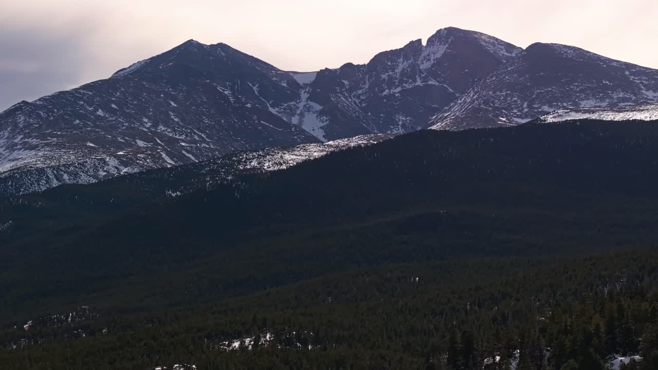 Aerial above alpine forest with rocky edges and snowy hillsides bathed in overcast light, Allenspark Colorado USA