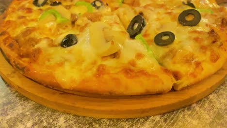 handheld orbiting shot around pizza with cheese and sliced olive