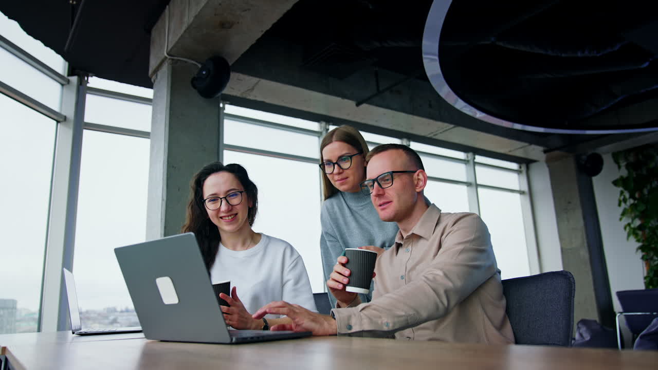 Lunch time in the office at workplaces. Three colleague drink coffee continuing work on laptop. Low angle view.