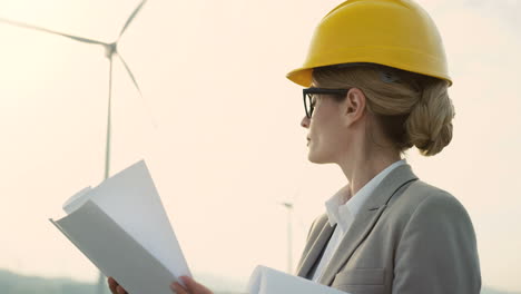 close-up view of caucasian woman engineer wearing a helmet watching some blueprints at wind station of renewable energy