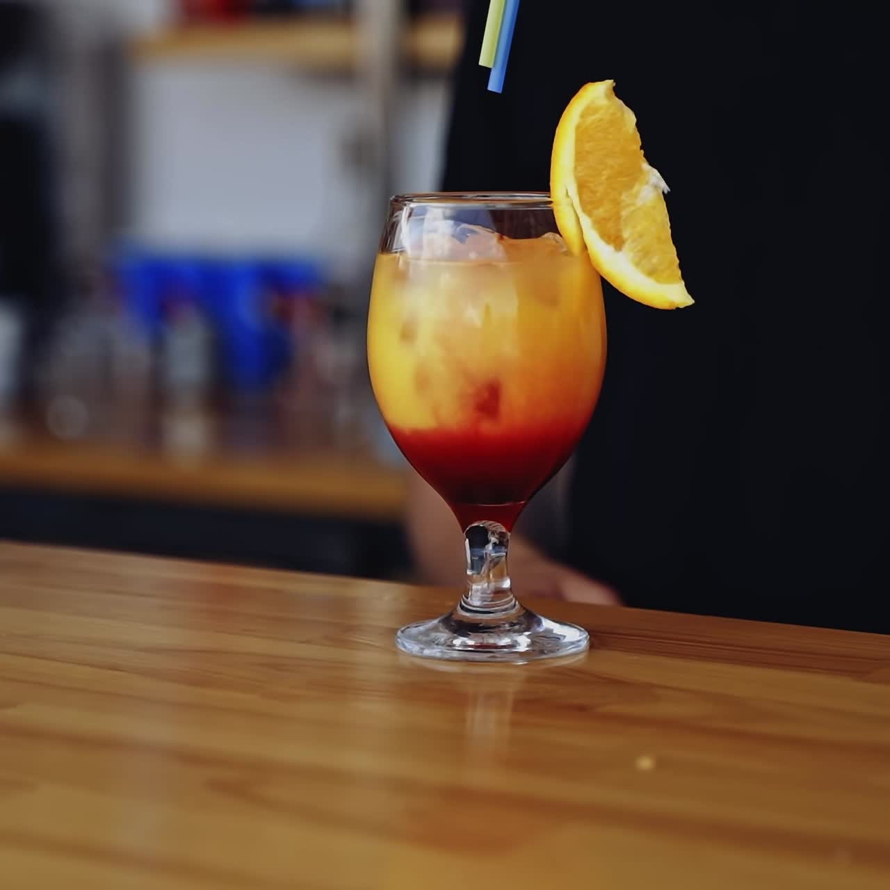 Tasty cocktail in glass. Bartender cooks the beverage for client. Fresh alcohol drink ready on a bar table. Slice of orange on a glass with color liquid with ice.