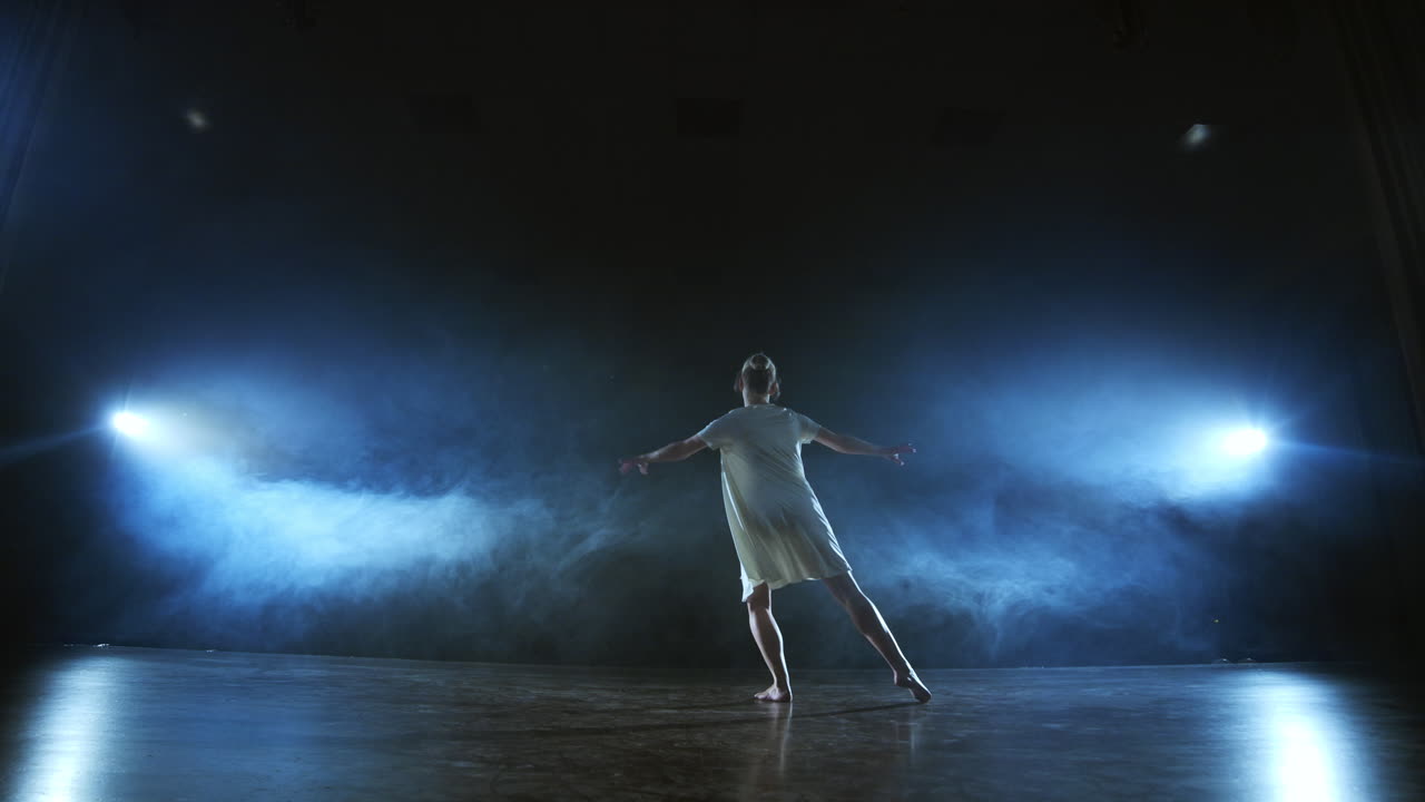 Modern ballet dancing woman barefoot doing spins and pirouettes and dance steps standing on stage in smoke in slow motion. Performance on stage.